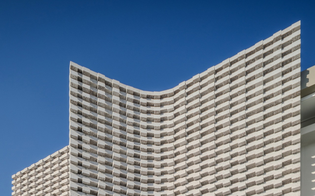 The curved façade demonstrates the material innovation that emerged from budget constraints, replacing the originally planned perforated steel