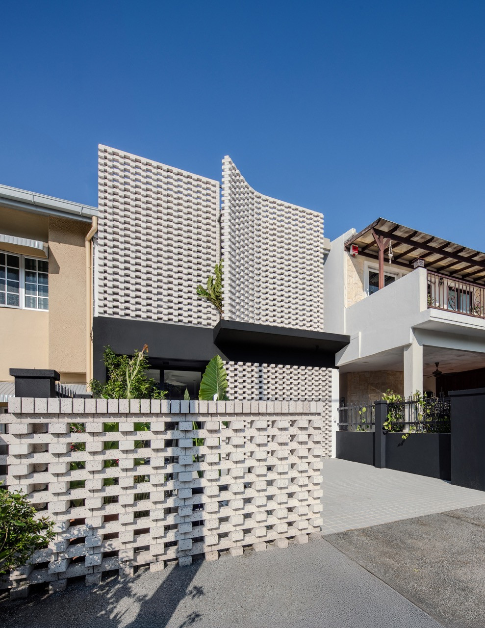 The façade curves and peels outward towards the front, opening the house to borrowed views of Bukit Tabur and enhancing the connection to the surrounding landscape