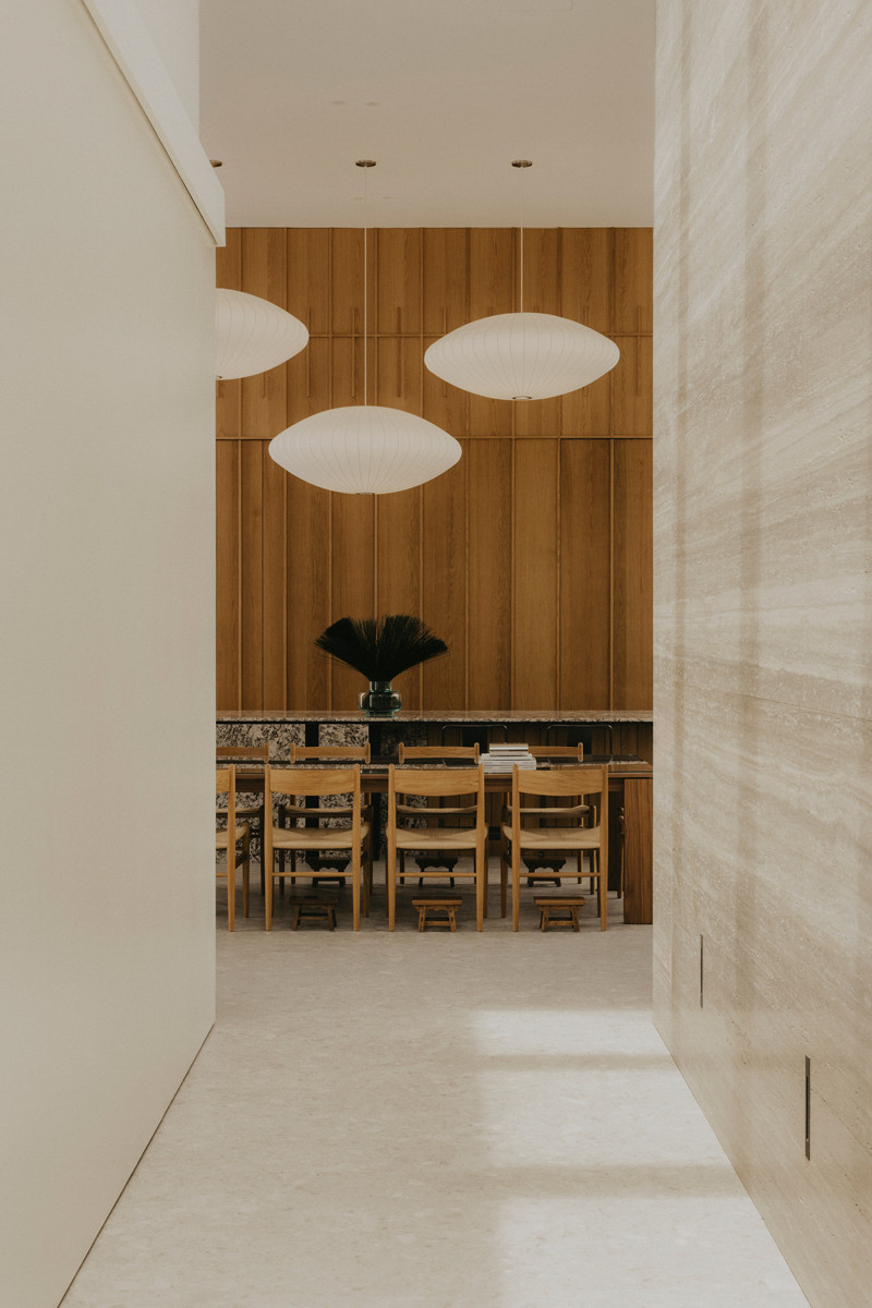 Viewed from the living area, the warm-toned dining rooms stands out agaisnt pale surfaces that frame it