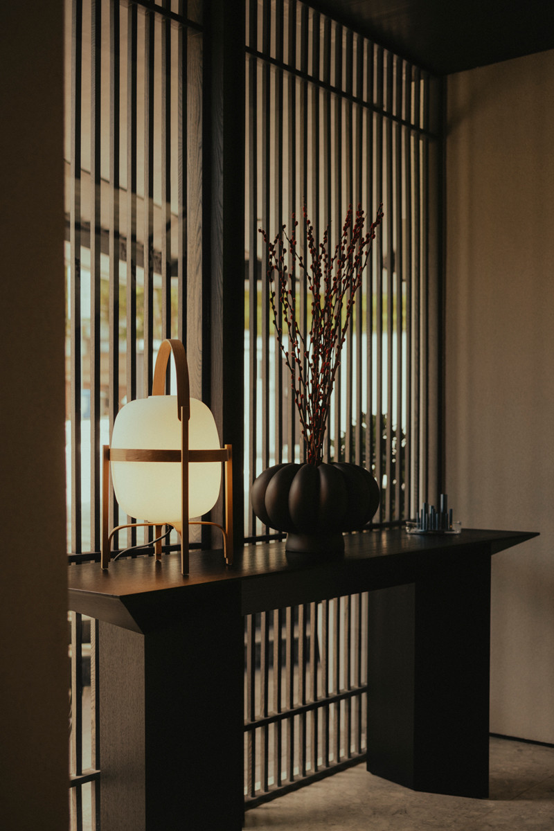 A well-curated tableau set in front of an architectural screen, comprising a Santa & Cole Cestita table lamp, 101 Copenhagen Kabin Lamella ceramic vase and Fritz Hansen Ikeru vase atop a geometric sideboard