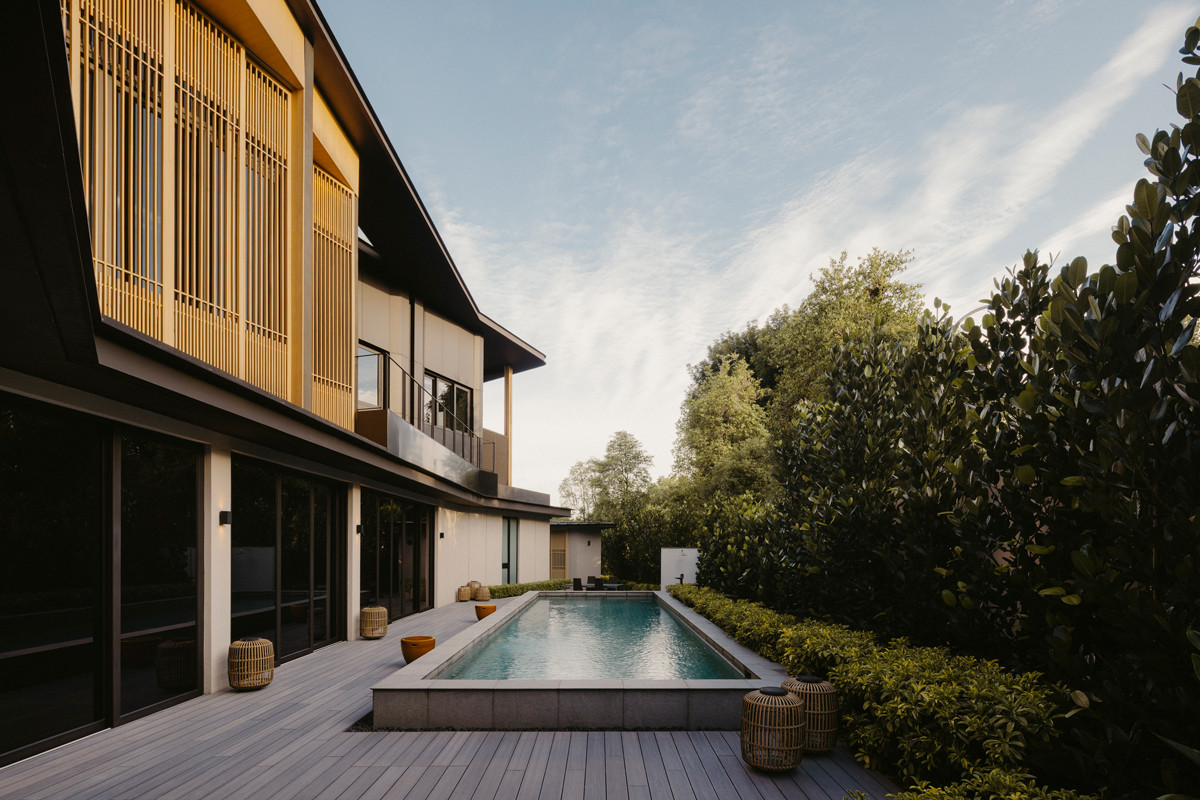 Along the pool’s edge, the side of the house unfolds in layers of timber and shadow, offering a softer, more intimate read of its heritage-inflected design