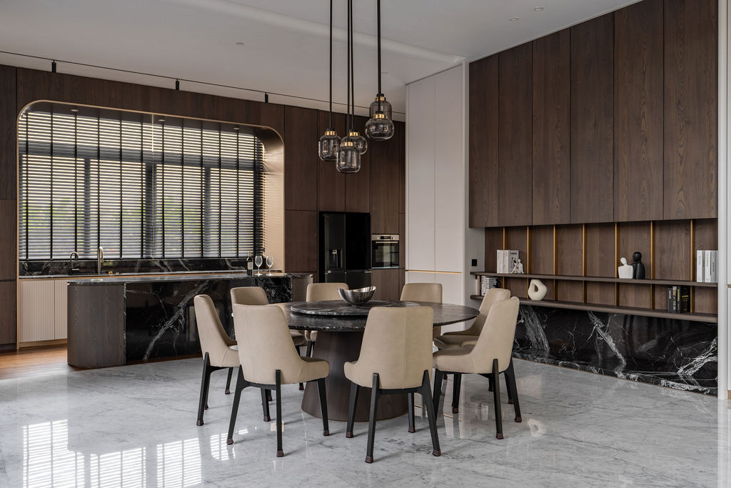 The dry kitchen extends the palette through dark wooden joinery with bronze trims and high-veined marble, whilst the rounded-edge island softens the rectilinear geometry