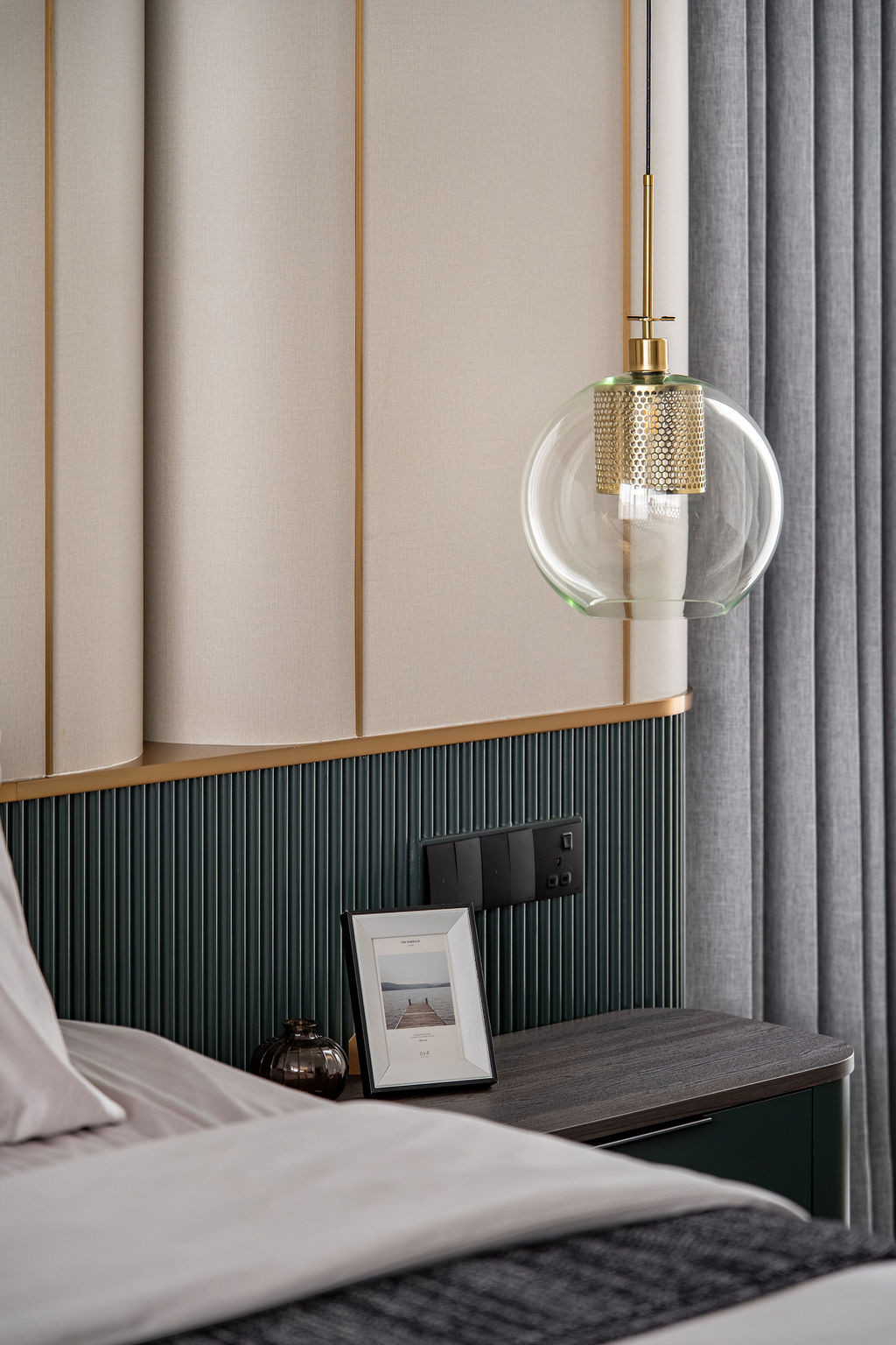 The master suite layers greige fabric panels with vertical brass trim alongside emerald ribbed detailing, establishing the calm environment through controlled materiality and precise bronze inlays