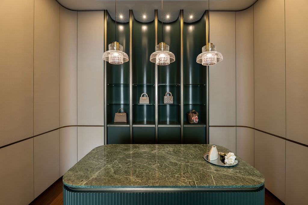 The dressing area adopts boutique retail language, integrating lacquered emerald panels with vertical brass trims and a central marble island featuring ribbed detailing and polished brass edging