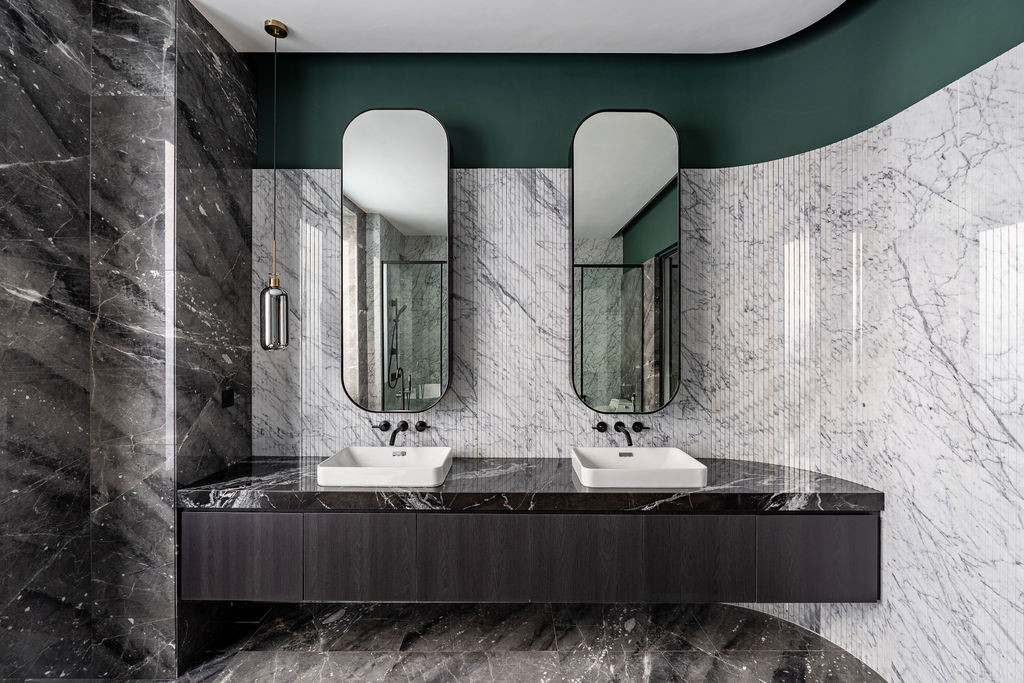 In the master bathroom, a double vanity in dark oak pairs with white-veining black marble, whilst a vertically fluted book-matched stone wall emphasises height and an emerald green feature plane establishes continuity with the dressing area palette