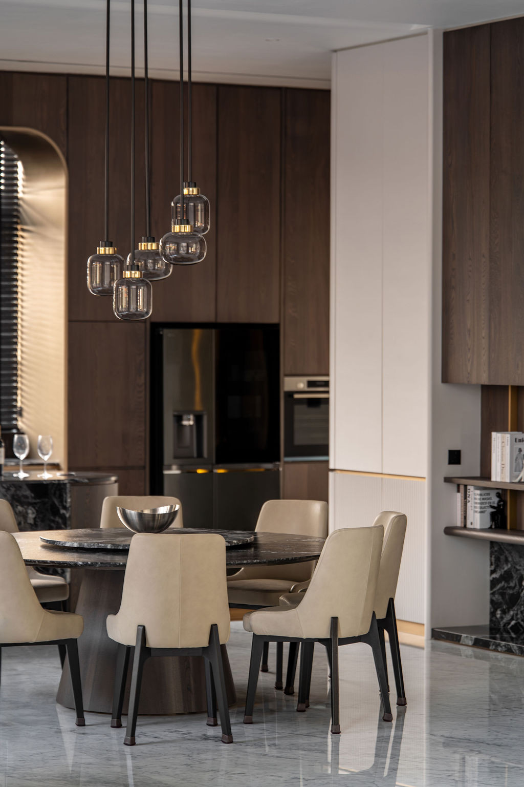 Clustered pendant lights with brass fittings suspend above the dining area’s dark marble table, maintaining sight lines to the entertainment room’s wet bar