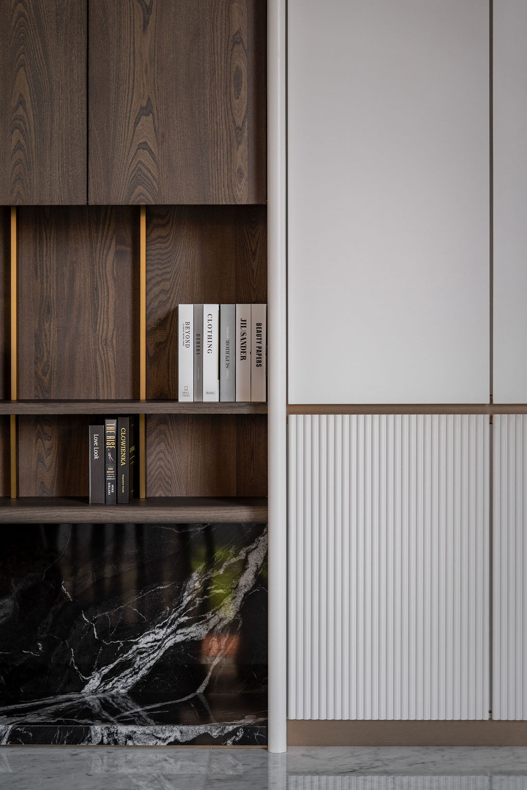 Open shelving in dark wood features vertical brass trims with integrated lighting, creating recessed niches that introduce rhythm and depth
