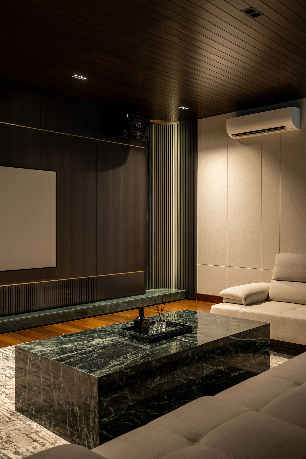 Charcoal cabinetry and green-veined marble establish the entertainment room’s atmosphere, with vertical trims and recessed niches introducing depth, whilst ambient lighting provides warmth