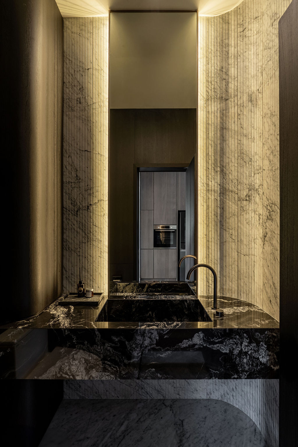 Vertically ribbed marble cladding is juxtaposed with integrated lighting behind a sculptural base with softened edges
