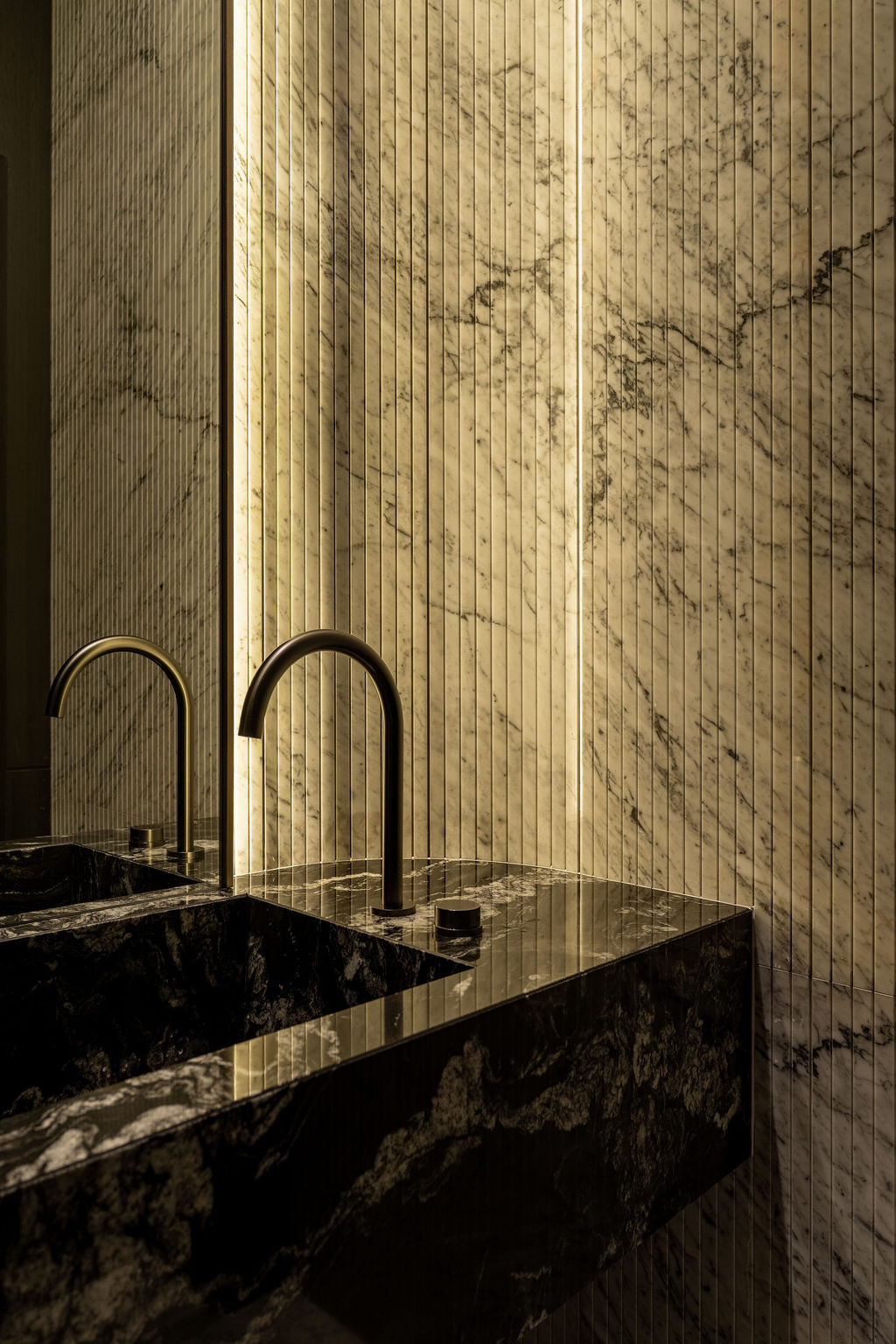 The powder room introduces soft curvature with full-height marble cladding featuring vertical ribbing, bronze taps, and curved timber panels concealing structural columns