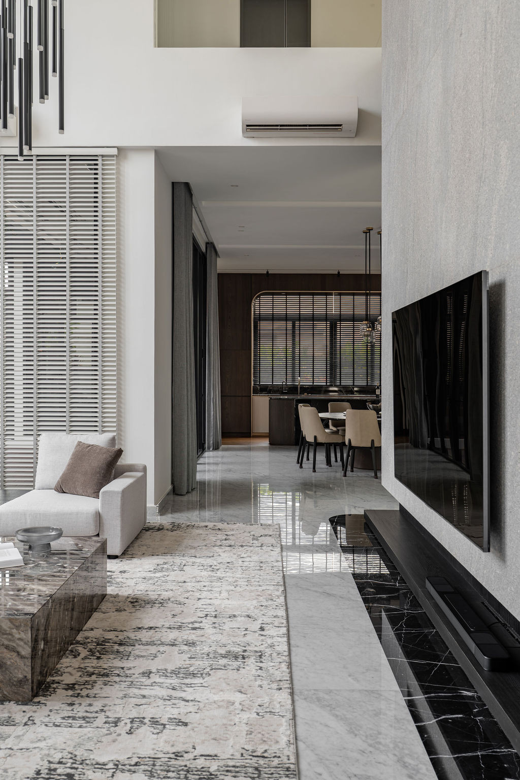 The double-height living space features a flamed granite wall with vertical wood detailing, maintaining sight lines through to the dining area and upper-level circulation