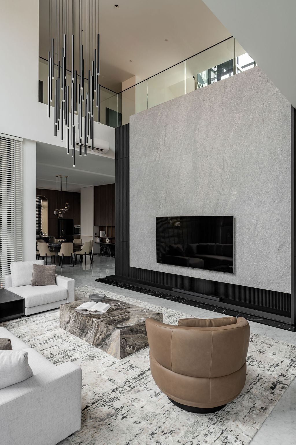 The living space is anchored by a flamed granite texture feature wall set against a double-volume ceiling, with a suspended linear chandelier accentuating the void and framing the primary seating zone