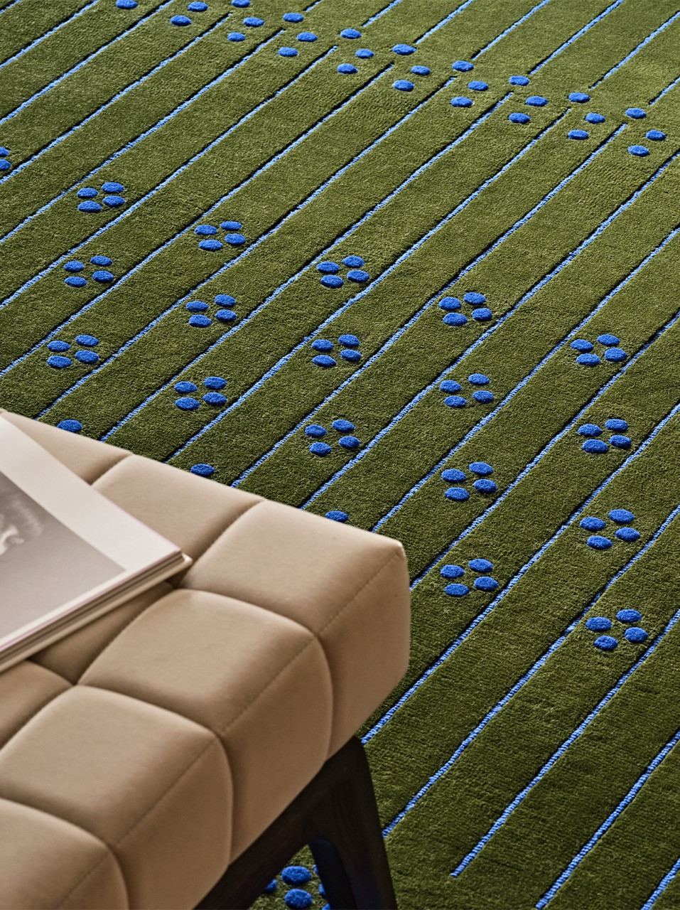 Najd references Riyadh's geometric Najdi architecture through diagonal green and cream stripes punctuated with blue circular motifs hand-knotted across the surface