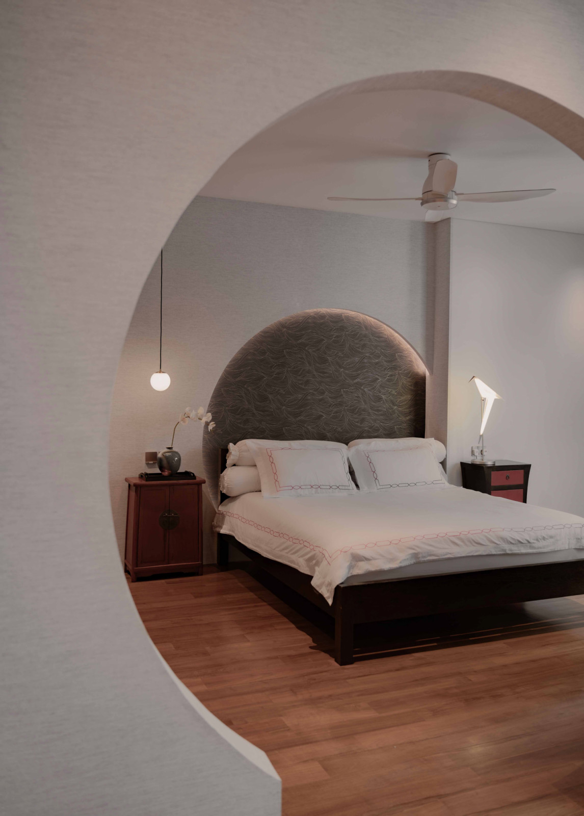 The master bedroom is framed by a circular moon-gate opening, echoed in the curved headboard to create a quiet visual alignmen