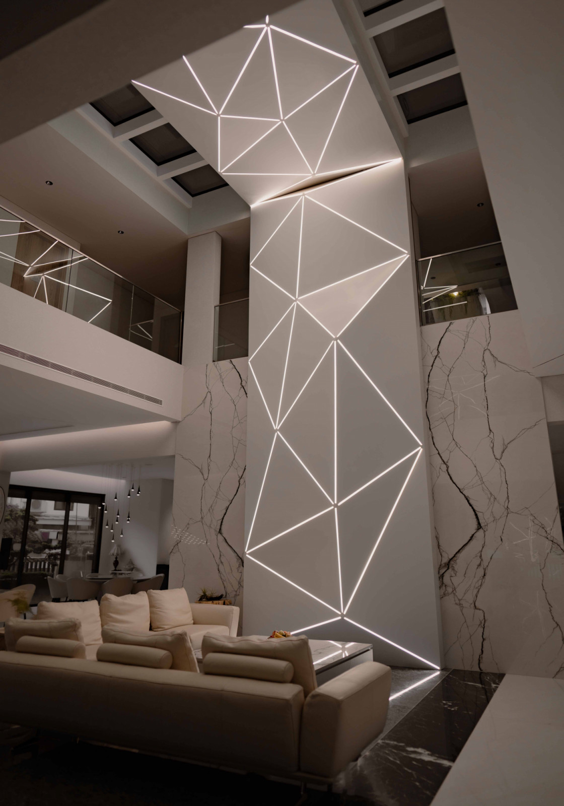 A geometric lighting installation wraps a structural column within the multigenerational home’s double-volume living space