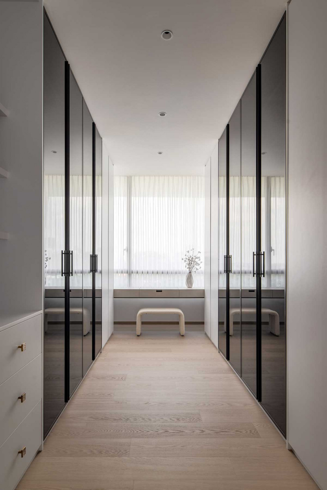 The spacious walk-in wardrobe is fitted with slim-framed glass doors and a cantilevered dressing table
