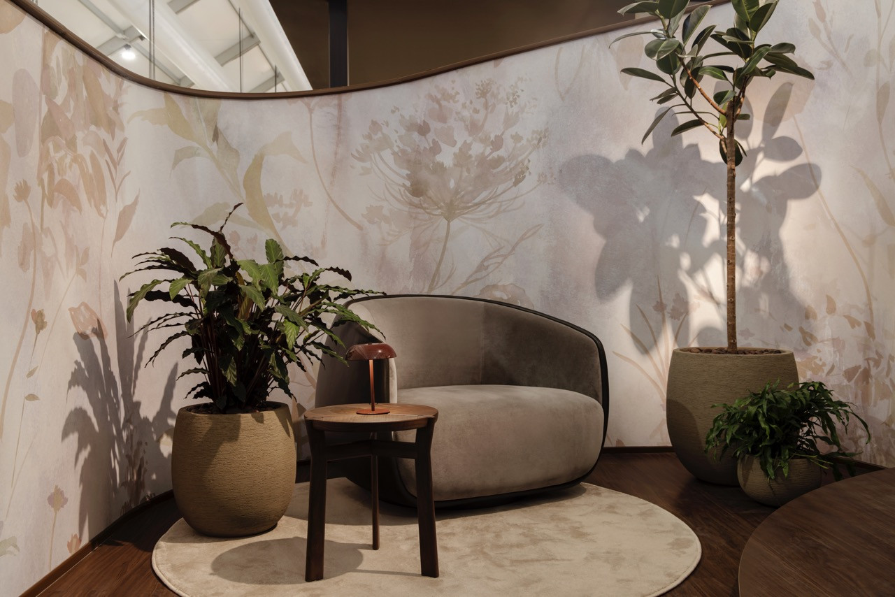 A reading nook features rounded seating against Calico Wallpaper’s large-scale botanical pattern, with layered planters creating an intimate residential atmosphere within the booth