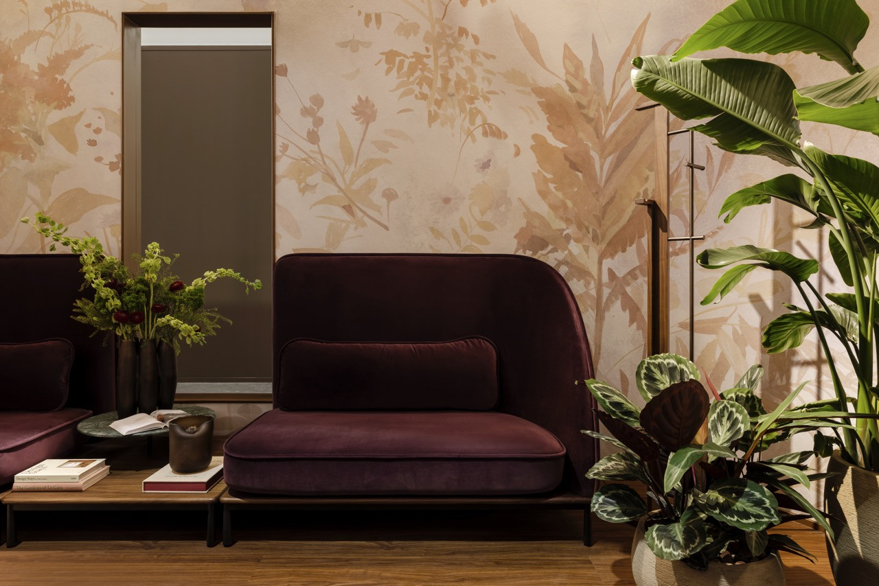 Alessandro Munge’s Marea seating in deep burgundy velvet positioned against Calico Wallpaper’s nature-inspired Arcadia pattern with brass mirror detail.