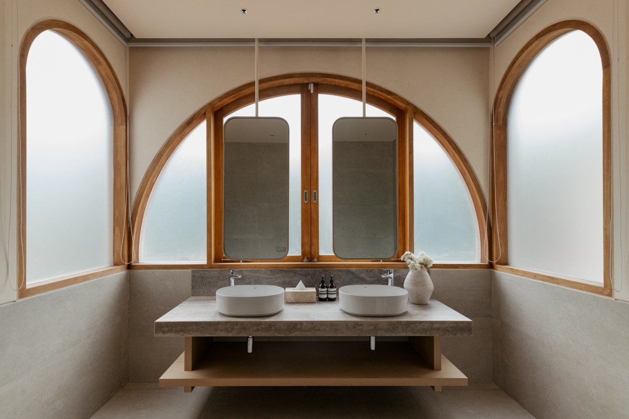Guest bathroom with arched timber-framed windows showing the natural material palette