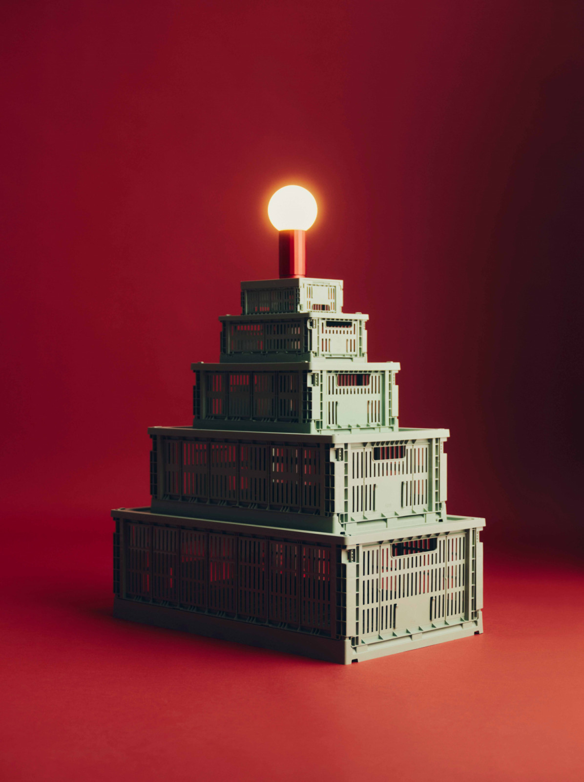 Stacked like a Christmas tree, the Hay Colour Crate and matching Colour Crate Lid in sage green are topped with the Turn On lamp in orange