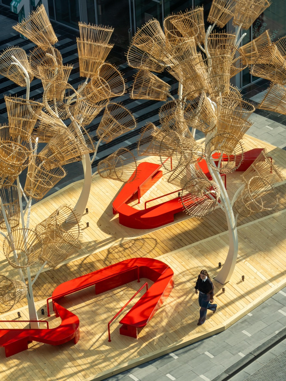 Aerial view of Designlab Experience installation at Dubai Design Week 2025 by Hibah Albakree, Mootassem El Baba and Marwan Maalouf, featuring red modular seating beneath woven palm frond canopy structures on wooden decking