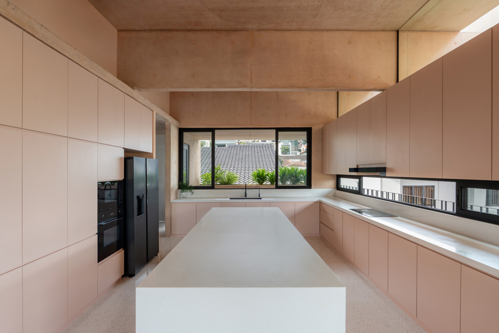 The kitchen occupies the third floor beneath the exposed pink concrete structure, where a horizontal window provides views