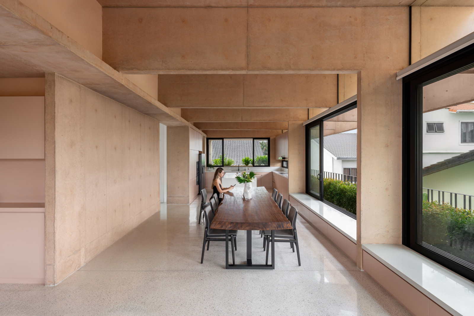 The third-floor dining area features exposed pink concrete beams running perpendicular to the side of the house