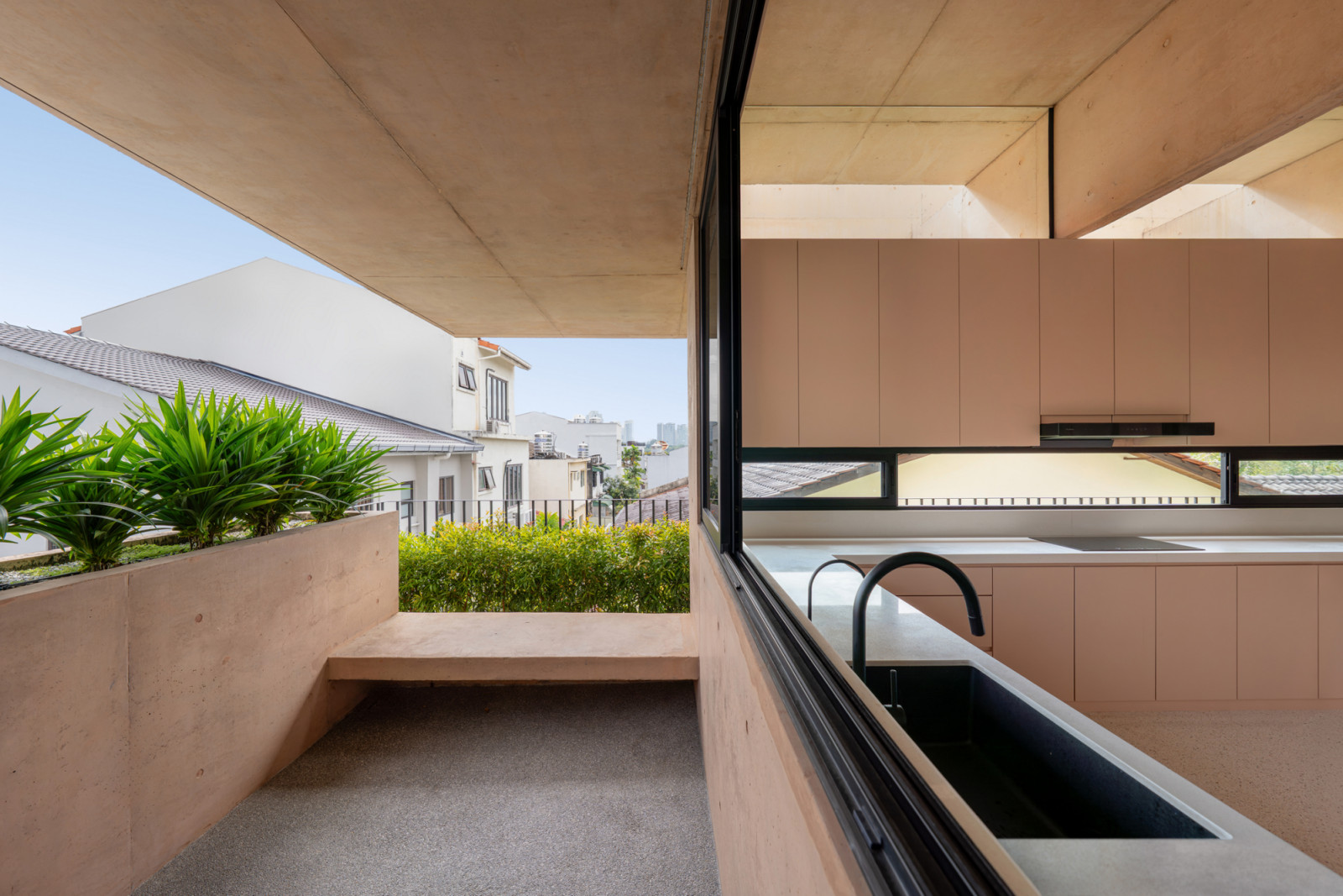 A built-in pink concrete bench extends from the kitchen onto the balcony, with the structural beams overhead extending the interior ceiling plane outward