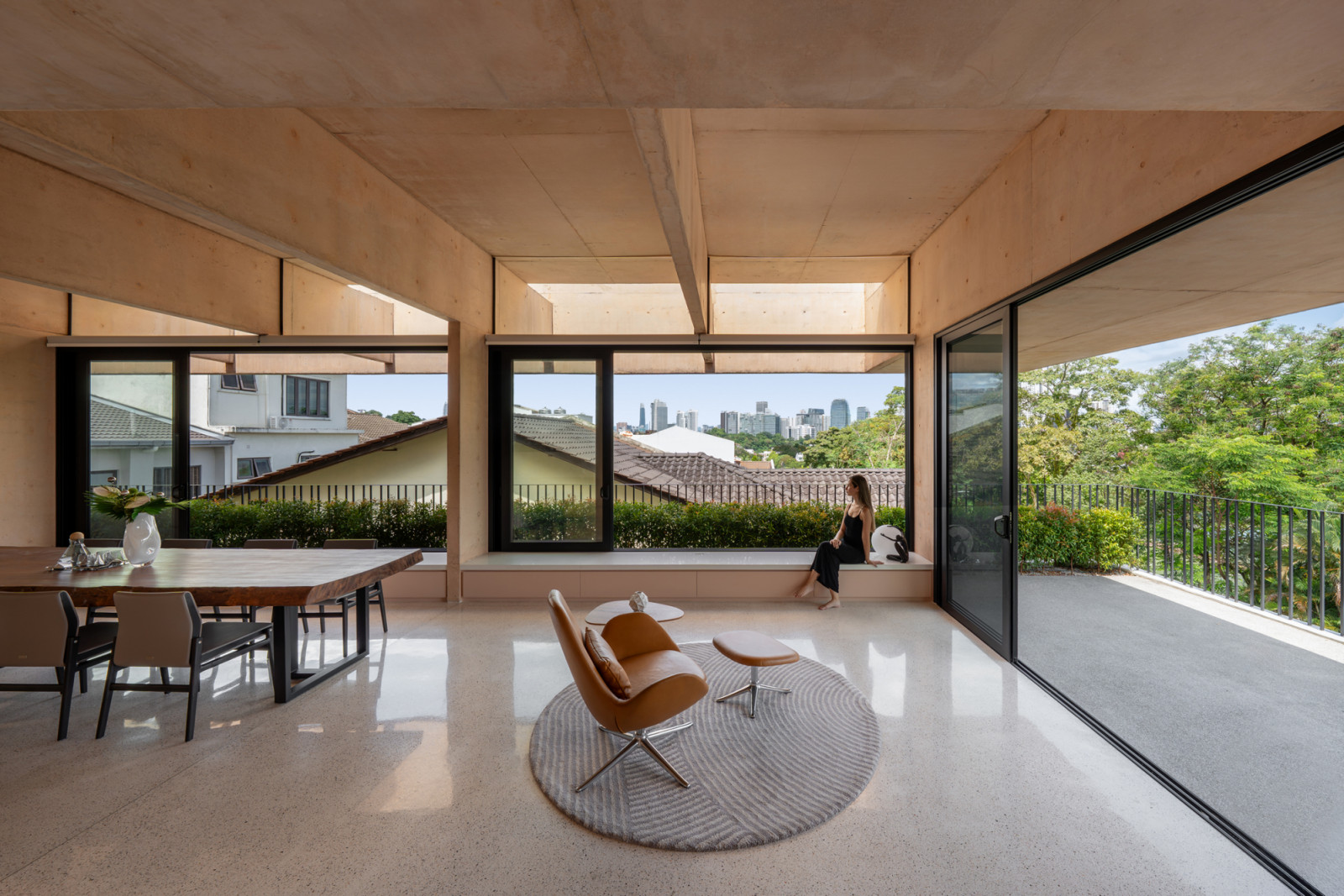 The third-floor living and dining area beneath the exposed pink concrete beam structure frames views across the treetops to the Kuala Lumpur skyline