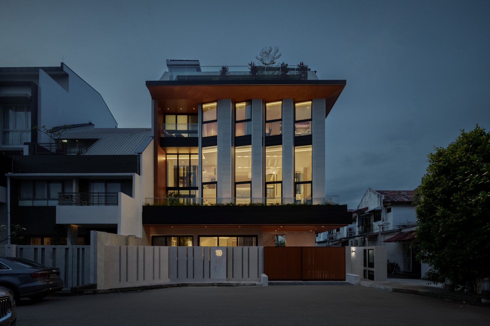 A roadside perspective of the house at dusk with windows aglow