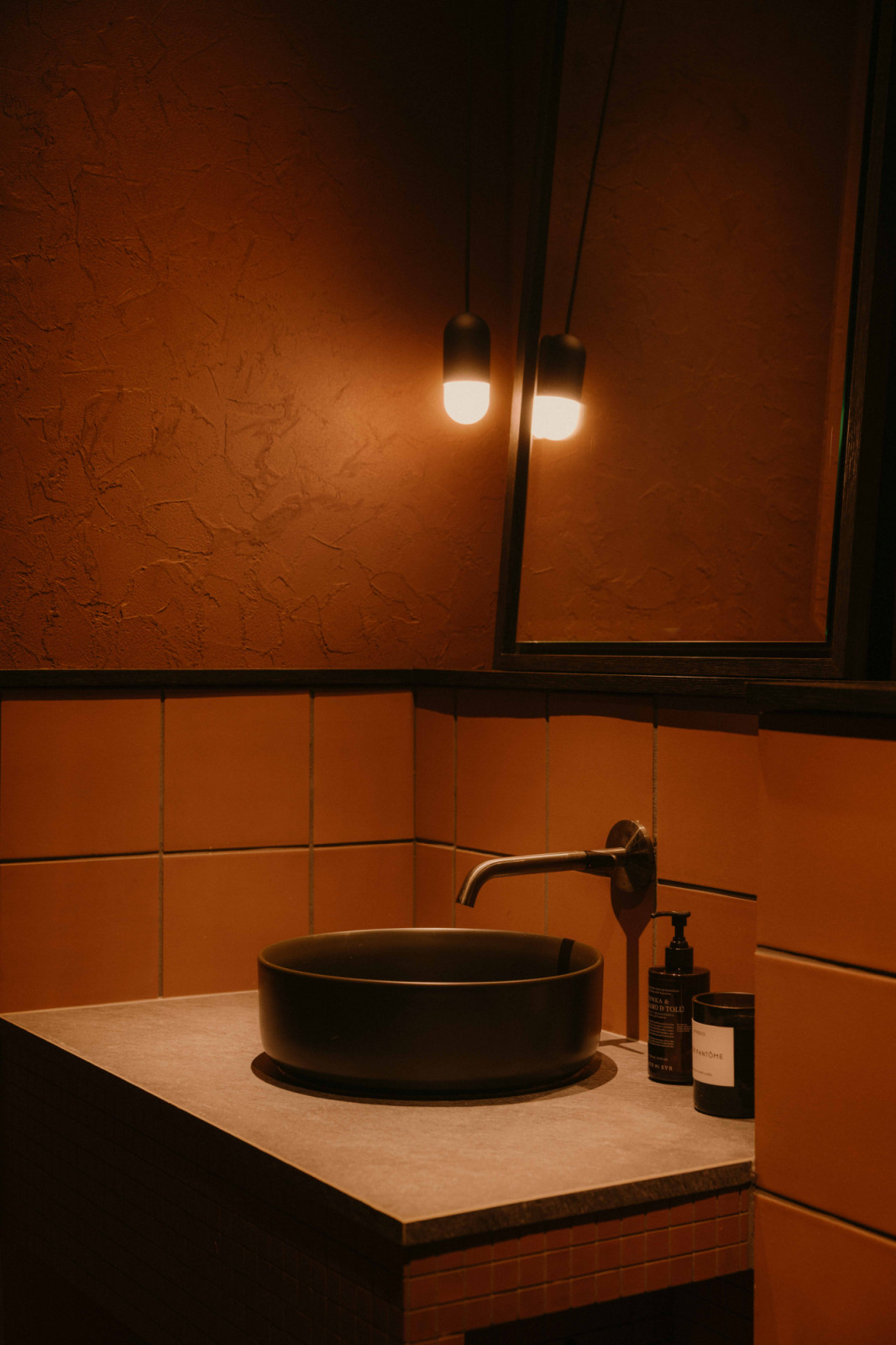 Echoing the kitchen, the powder room adopts a moody lighting and palette inspired by restaurant settings