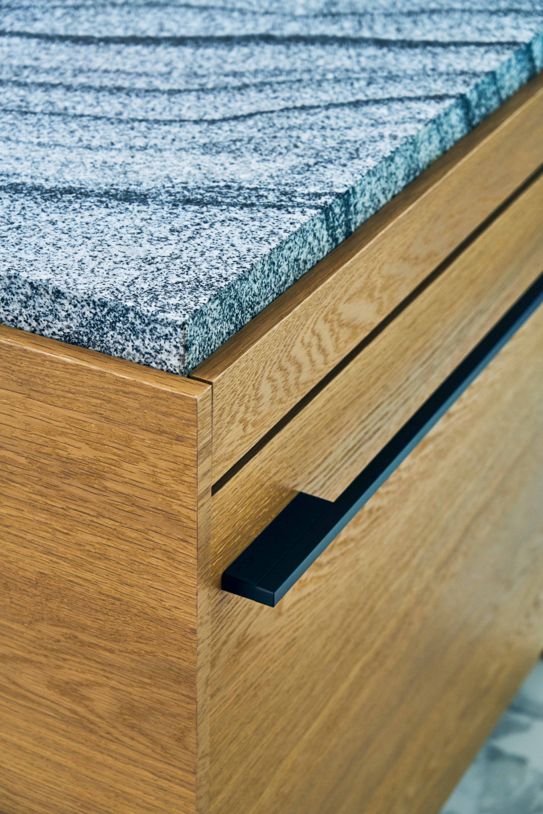 A close-up detail of the kitchen counter highlights the junction between speckled stone and timber