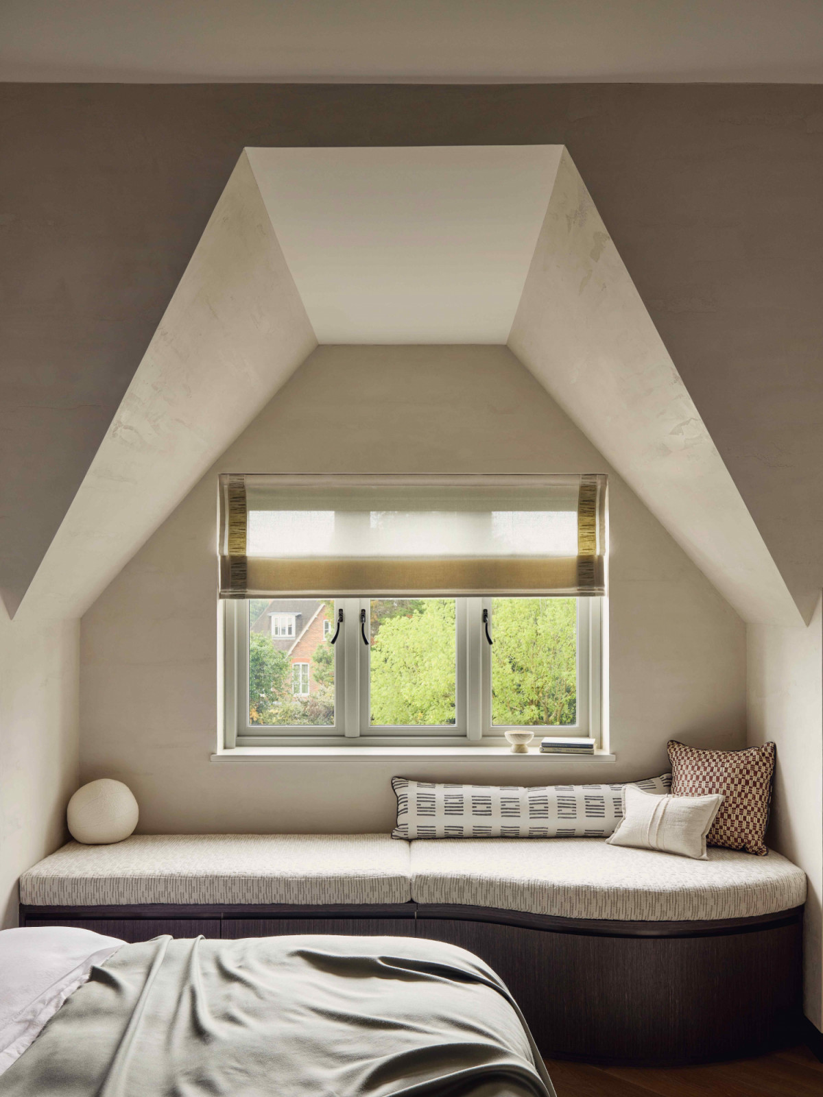 A custom window seat with upholstered cushion by Zak+Fox wedged under the slanted ceiling