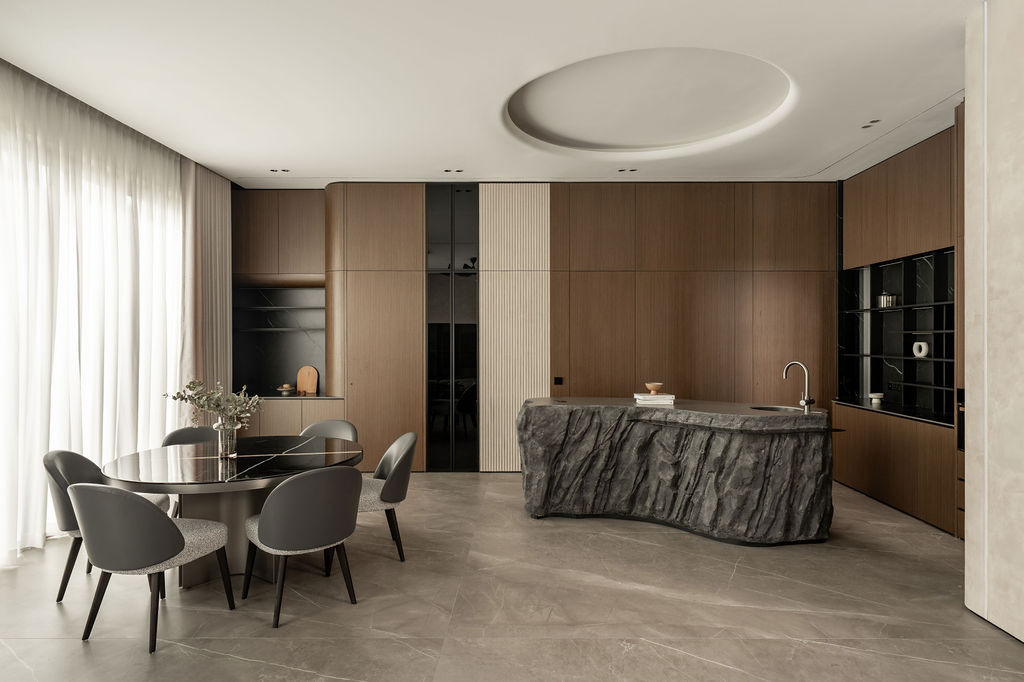The dining and kitchen area showcases the balance between micro-cement surfaces, timber cabinetry, and the crafted stone island