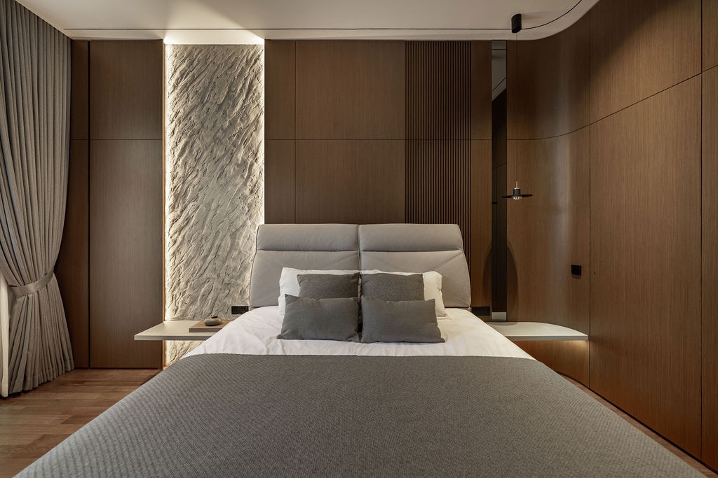 Timber cabinetry wraps the bedroom with a backlit textured stone accent panel