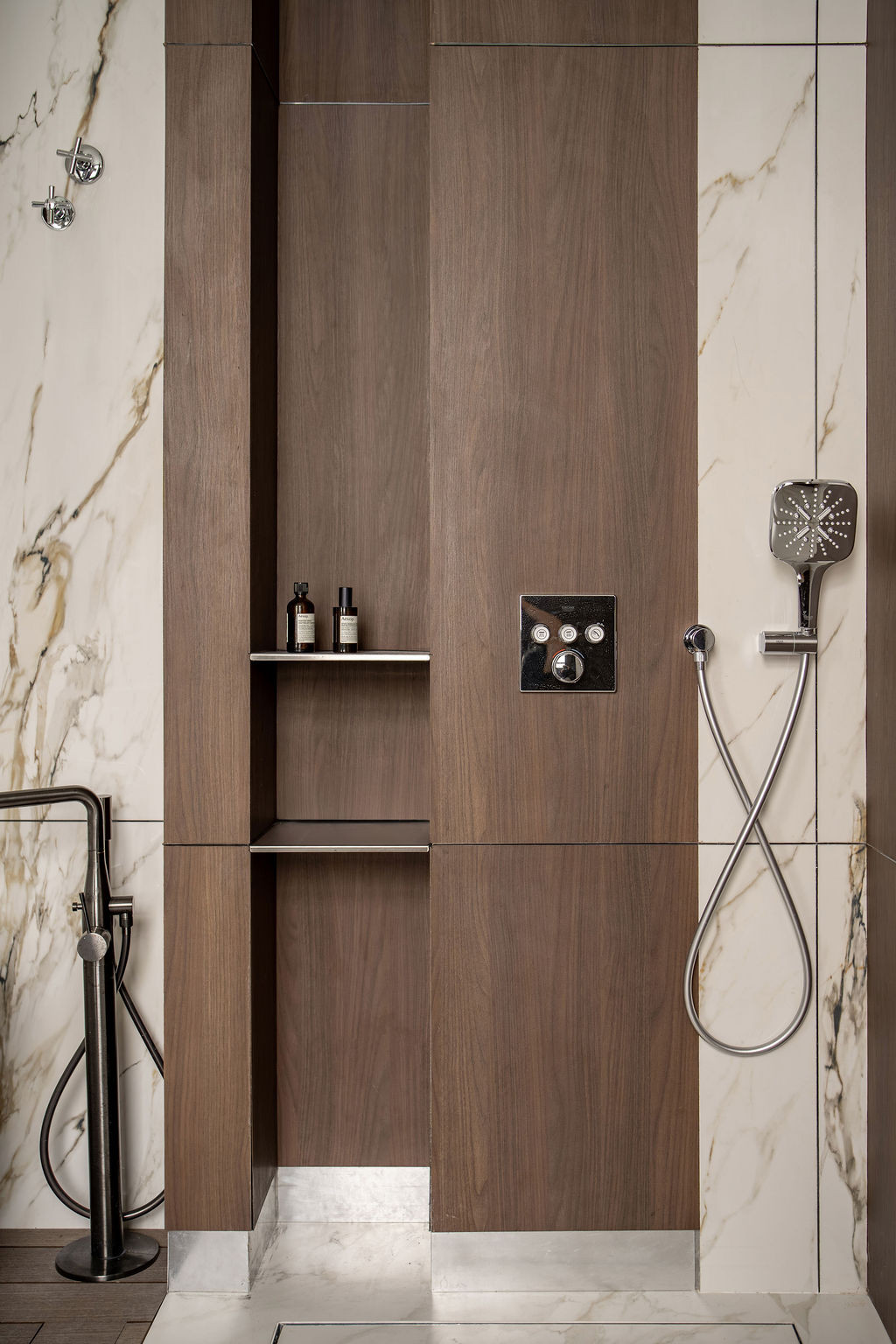 Timber shower niches are integrated into marble-clad bathroom walls with recessed shelving for storage