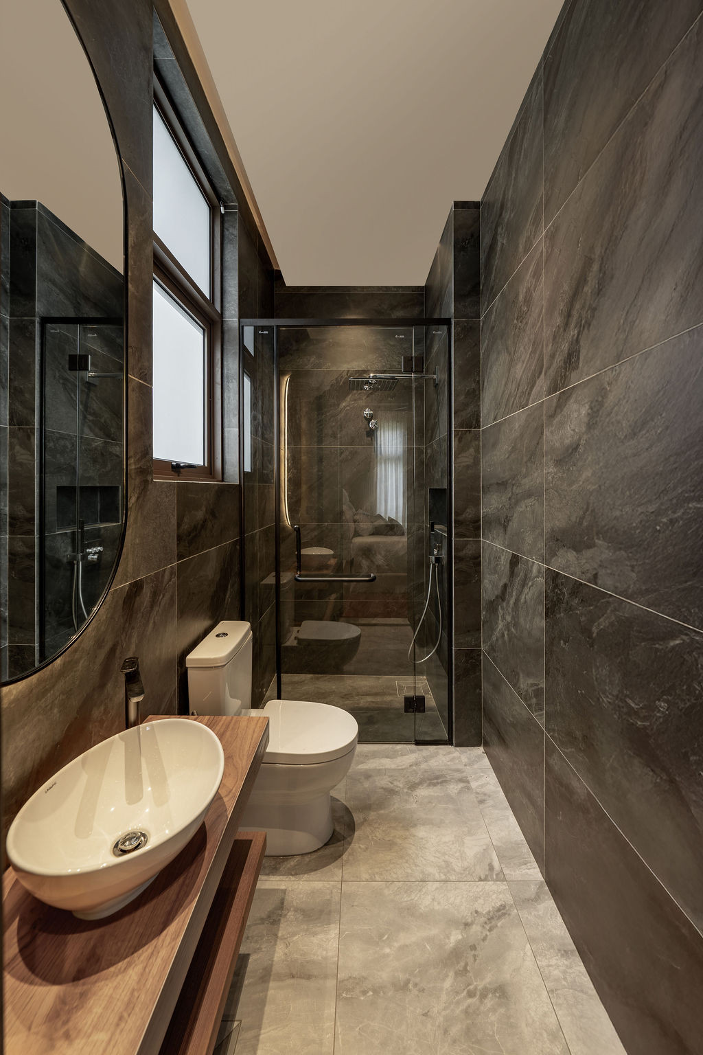 The bathroom combines dark stone tiles with timber vanity elements and concealed lighting