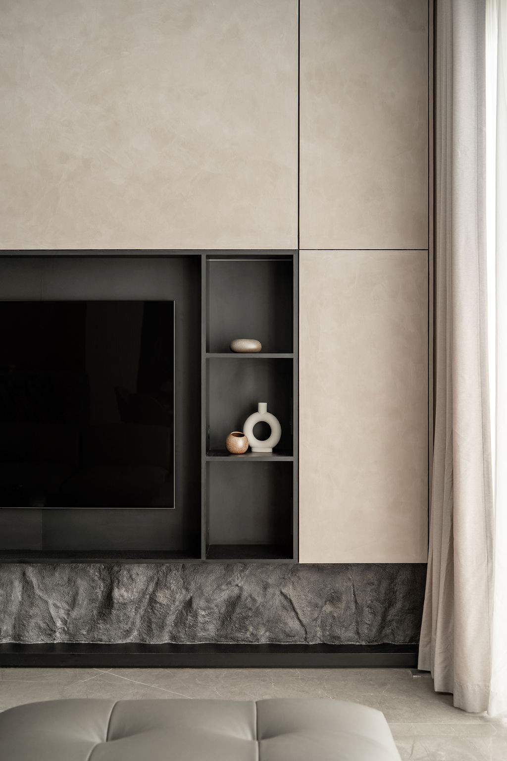 Micro-cement panels frame the television niche with its textured stone base and recessed dark display shelving