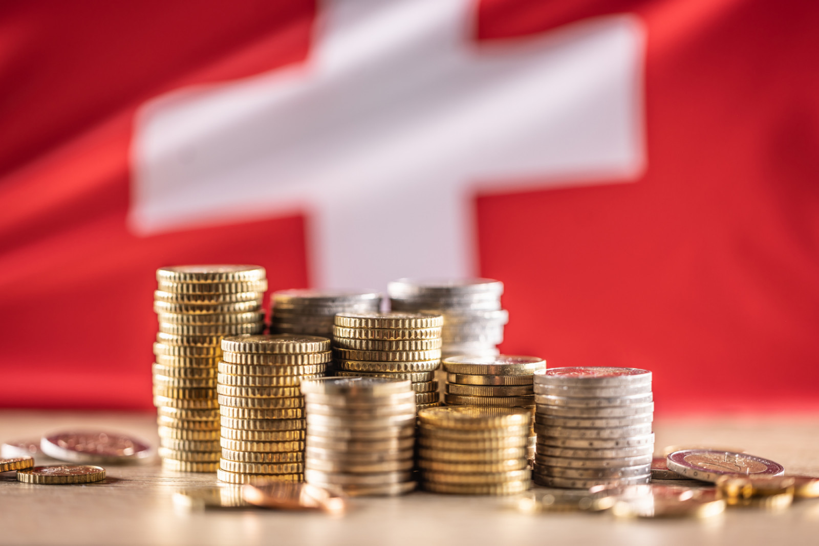 Euro coins stacked on top of each other in different positions in front of the Swiss flag. Finance Business and Economy Concept. (photo: SimpleImages / Getty Images)