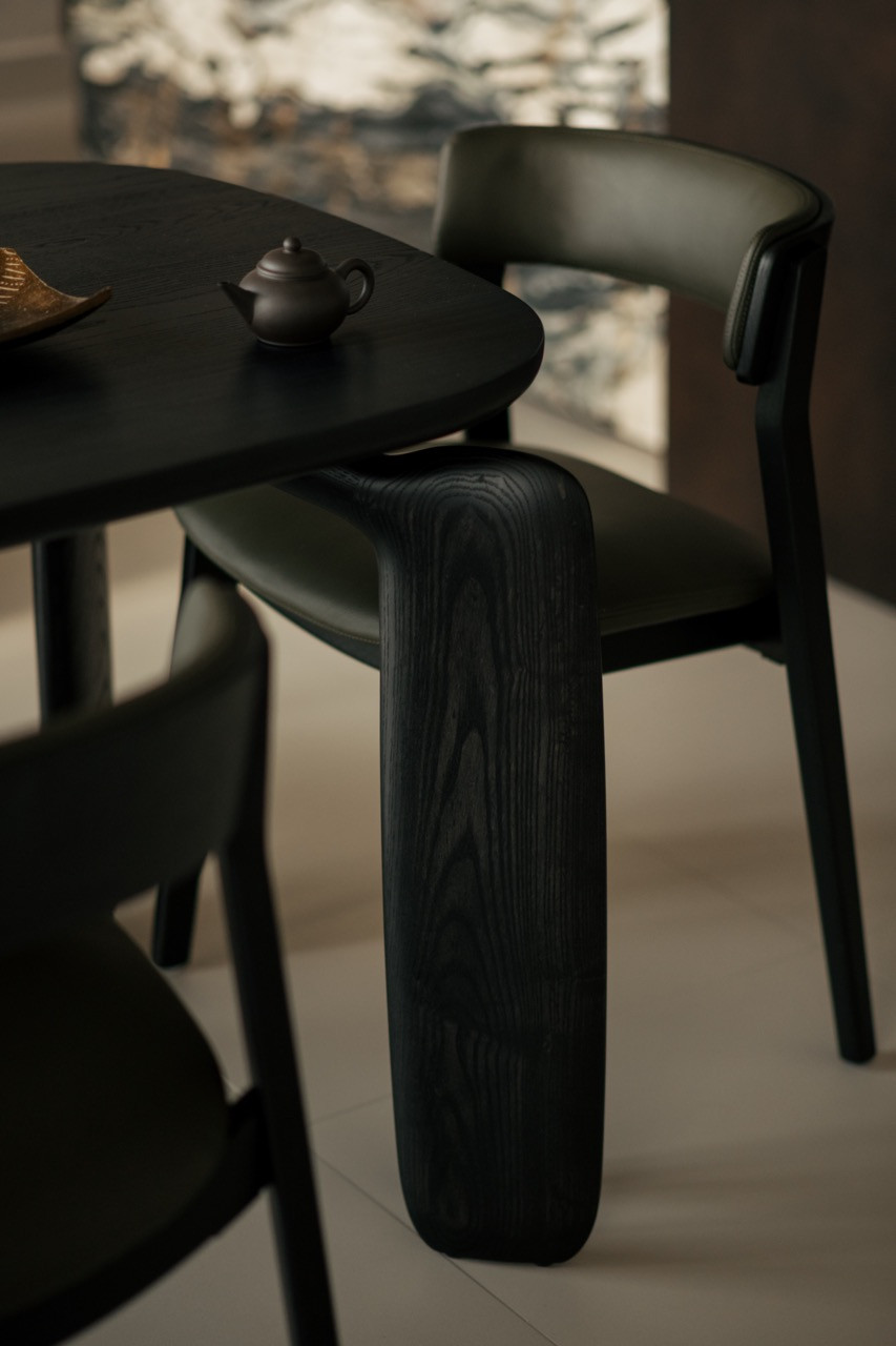 Black-stained dining chairs with leather upholstery sit beside the circular table, sourced from King Living
