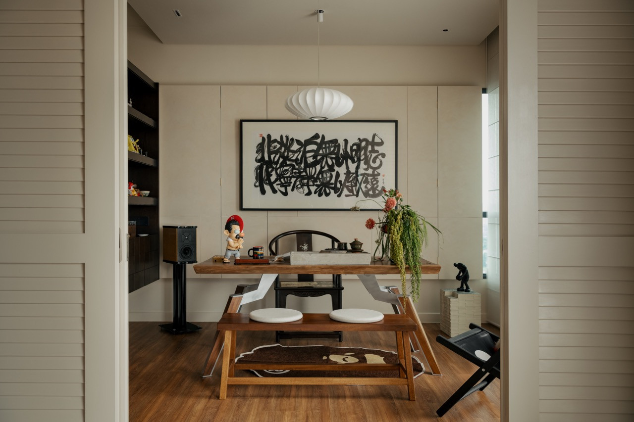 The dining area features a wooden table beneath a piece of calligraphy art and a bubble pendant light, with the home office visible through louvre doors