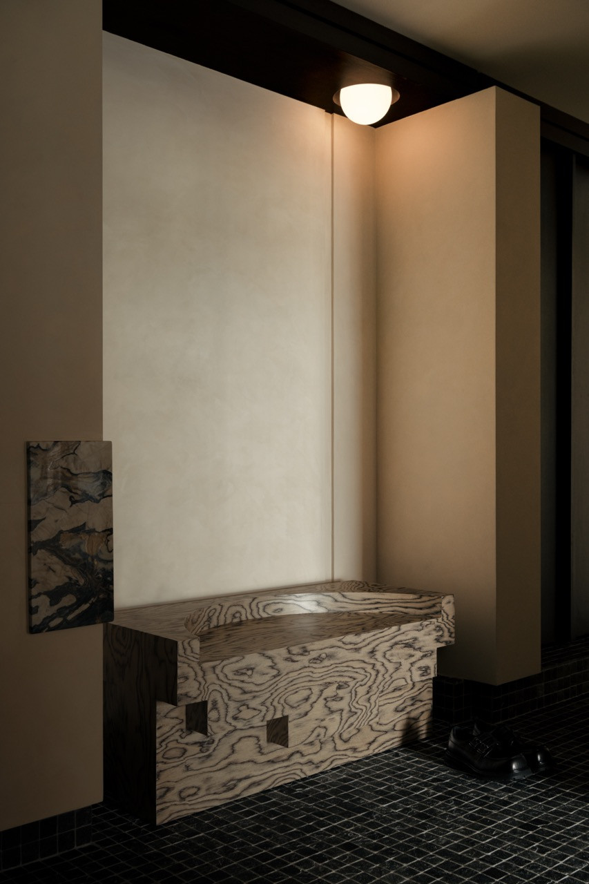 The custom-designed bench in special veneer finish sits on silver quartz mosaic flooring near the entrance