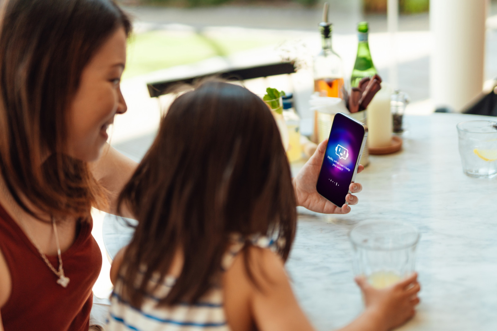 Young Asian mother and daughter speaking to virtual assistant via AI chatbot app on smartphone. Open AI technology. Online robot system.