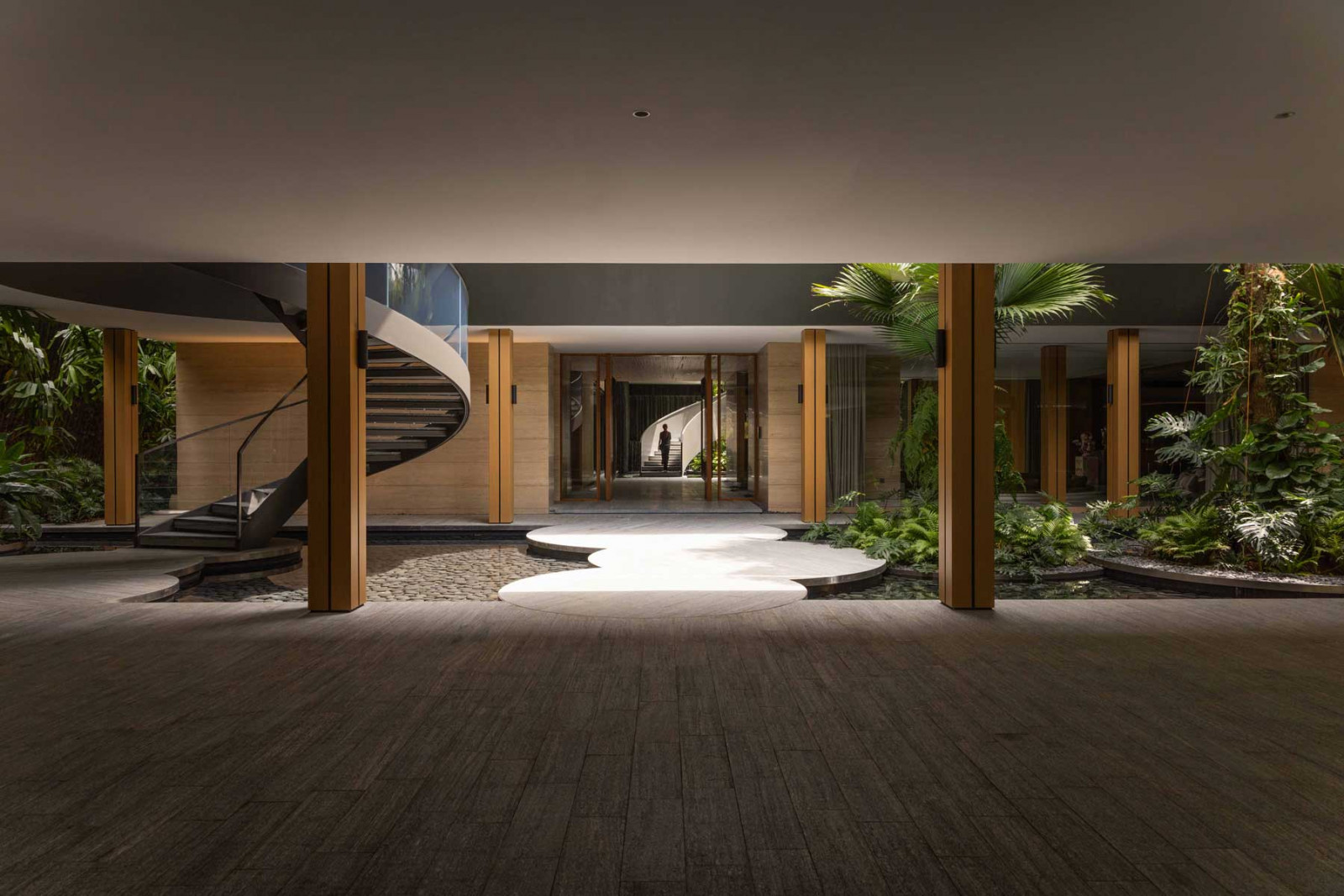 A sequence of circular stepping stones leads across the courtyard to a sculptural spiral staircase, embodying the house’s play of compression and release, shadow and light