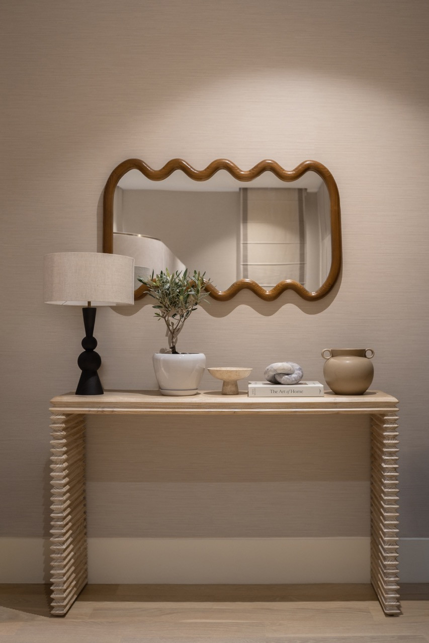 A hallway console with sculptural details features a wavy-edged wood mirror above a table with curved legs