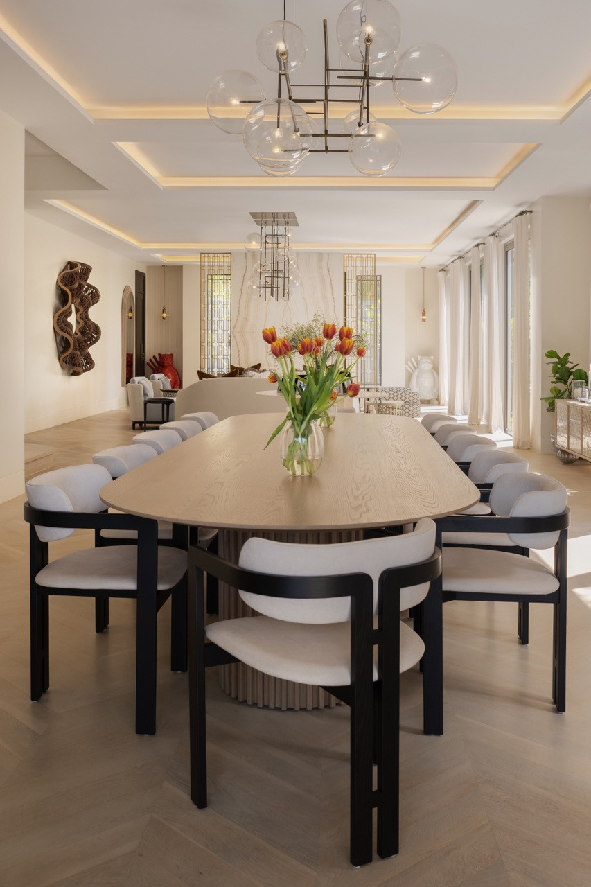 The oval dining table seats ten beneath a geometric chandelier, with views through to the formal living room’s marble wall