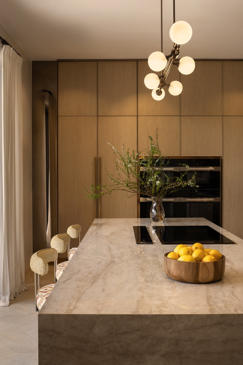 The kitchen island seats up to eight on boucle upholstered bar stools beneath a Sputnik-style chandelier