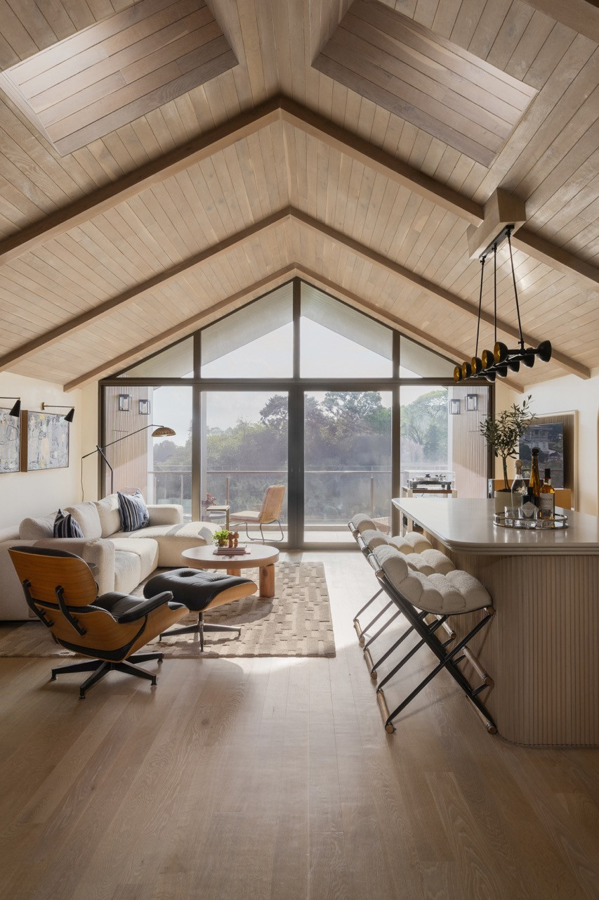 Tâm điểm của không gian thư giãn này là khung cửa sổ đầu hồi (gabled window) hướng trọn tầm nhìn ra sân vườn xanh mát, với khu vực quầy bar được bố trí khéo léo về một phía để tạo sự khoáng đạt cho khu vực trung tâm.