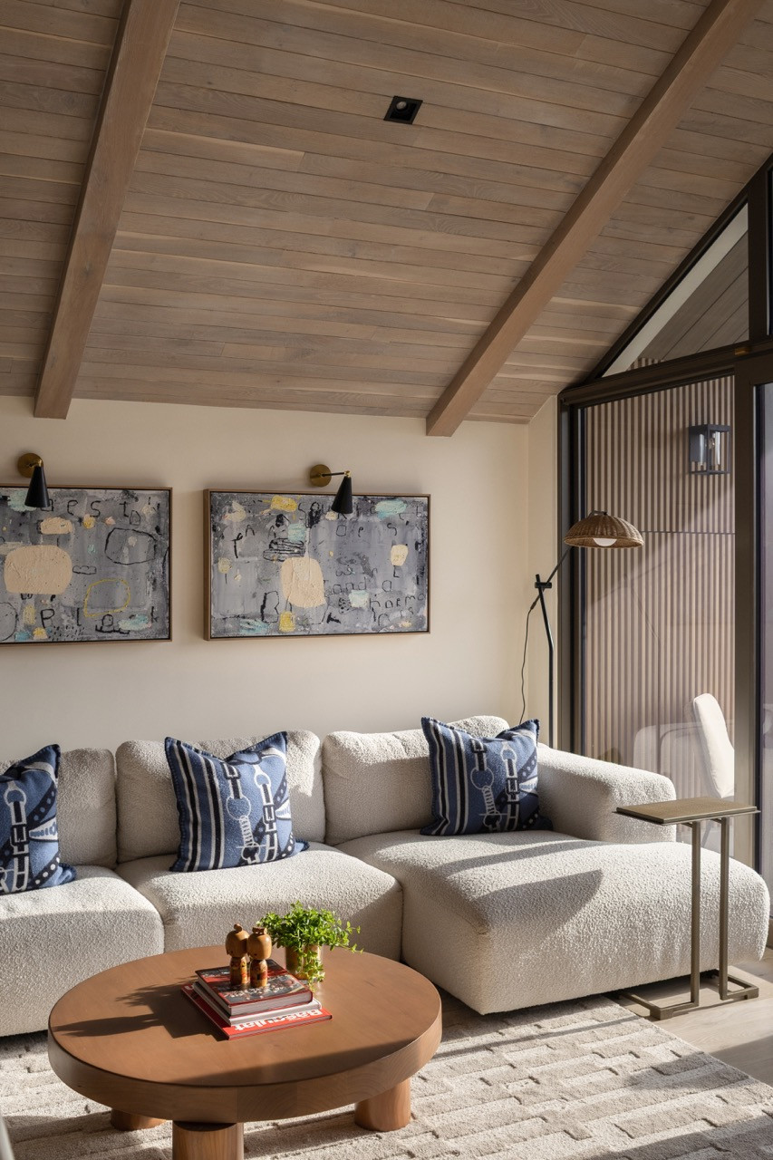 Góc thư giãn đầy mời gọi với chiếc sofa bọc vải boucle mềm mại, được đặt tĩnh tại dưới hệ trần gỗ uốn vòm và điểm xuyết bởi những tác phẩm nghệ thuật đương đại.