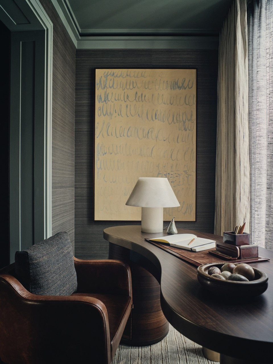 The study features abaca wallpaper by Mark Alexander and a curved, dark-wood desk with bronze detailing, handcrafted in Italy